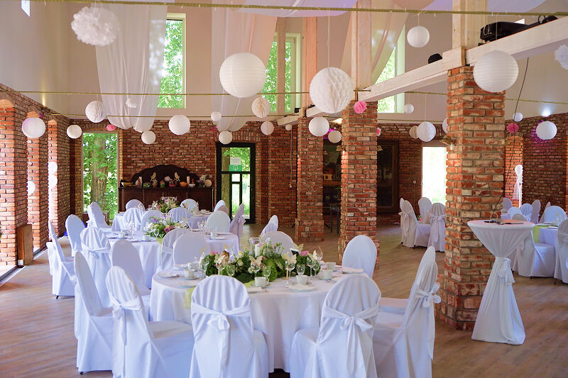 Eventscheune, Weitwinkel-Aufnahme. Dekorationen in Pink und viel Grün. Weiße Bezüge für Tische und Stühle.