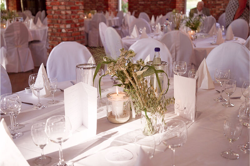 Eventscheune, Tisch-Dekorationen. Sehr viel Weiß. Etwas Beige. Verschiedene Gräser in einem Glas.