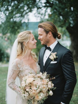 Hochzeitspaar sieht sich liebevoll in die Augen. Im Hintergrund Wiese und Baum.