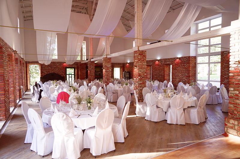 Eventscheune, Weitwinkel-Aufnahme. Dekorationen in Weiß und Pink. Weiße Bezüge auf Tischen und Stühlen..